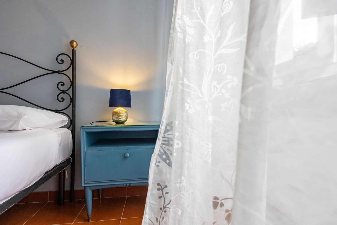 Un dormitorio con una cama, una mesita de noche con lámpara y una cortina.