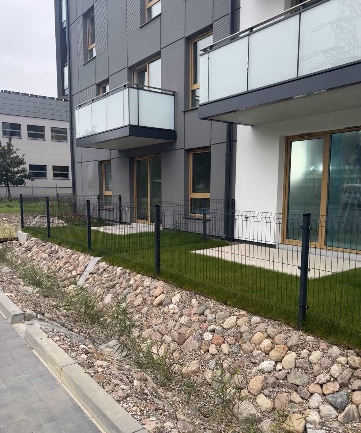 A modern building with a balcony, a stone retaining wall, and a metal fence.