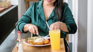 Une personne est assise à une table devant une assiette de nourriture et un verre de jus d’orange.