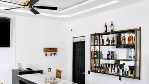 Un espace bar moderne doté d’un comptoir en marbre, de chaises en bois, d’un ventilateur de plafond et d’un présentoir pour les boissons alcoolisées.