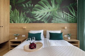 Een hotelkamer met een groot bed, twee nachtkastjes, een houten hoofdbord en een wanddecoratie met tropische bladeren.