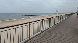 Una pasarela de madera con barandas de metal que lleva a una playa de arena y al océano.