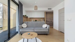 Una sala de estar moderna con un sofá gris, una mesa de centro redonda de madera y un ventanal grande.