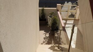 Eine Treppe in Beige führt zu einem Balkon mit Geländer, einem kleinen Topfpflanzen und freiem Blick auf die Straße darunter.