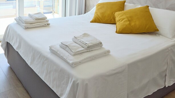 Ein Hotelzimmer mit einem großen Bett, zwei Kissen, ordentlich gefalteten Handtüchern, einer Wandleuchte und Blick auf den Außenbalkon.