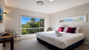 A hotel room with a large bed, a desk, a chair, and a window with a view of trees and mountains. - Heated Plunge Pool with Bay Views! (WAGSTAFFE)