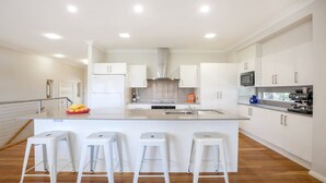 Una cocina moderna con armarios blancos, una isla central con taburetes, horno empotrado y microondas.
