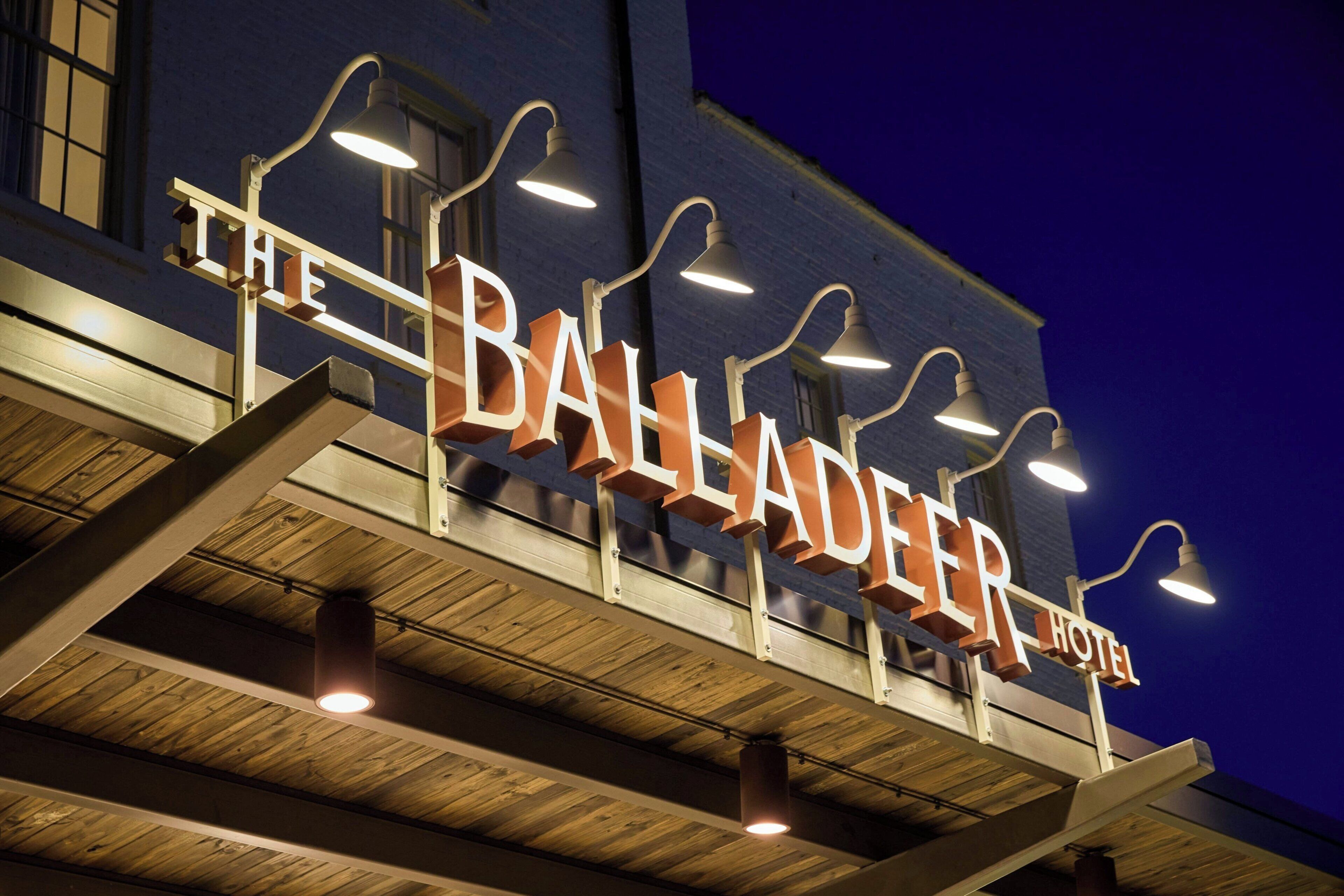 En hotellskylt med namnet ”The Balladeer Hotel”, upplyst av lampor som hänger ovanför.