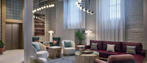A modern hotel lobby with a seating area, a sofa, a coffee table, and a plant.