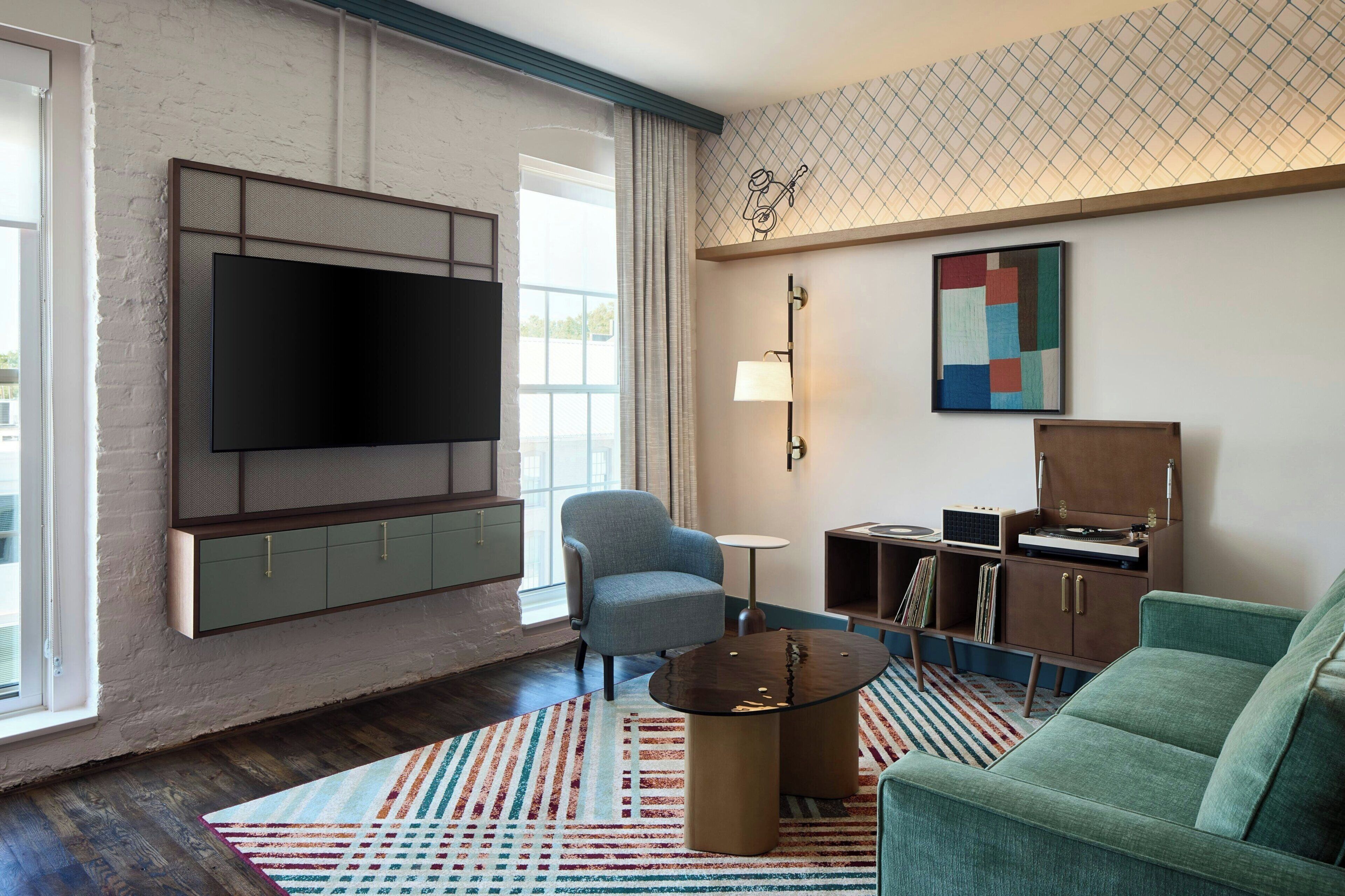 A modern living room with a flat-screen TV, a blue armchair, a green sofa, a coffee table, and a patterned rug.