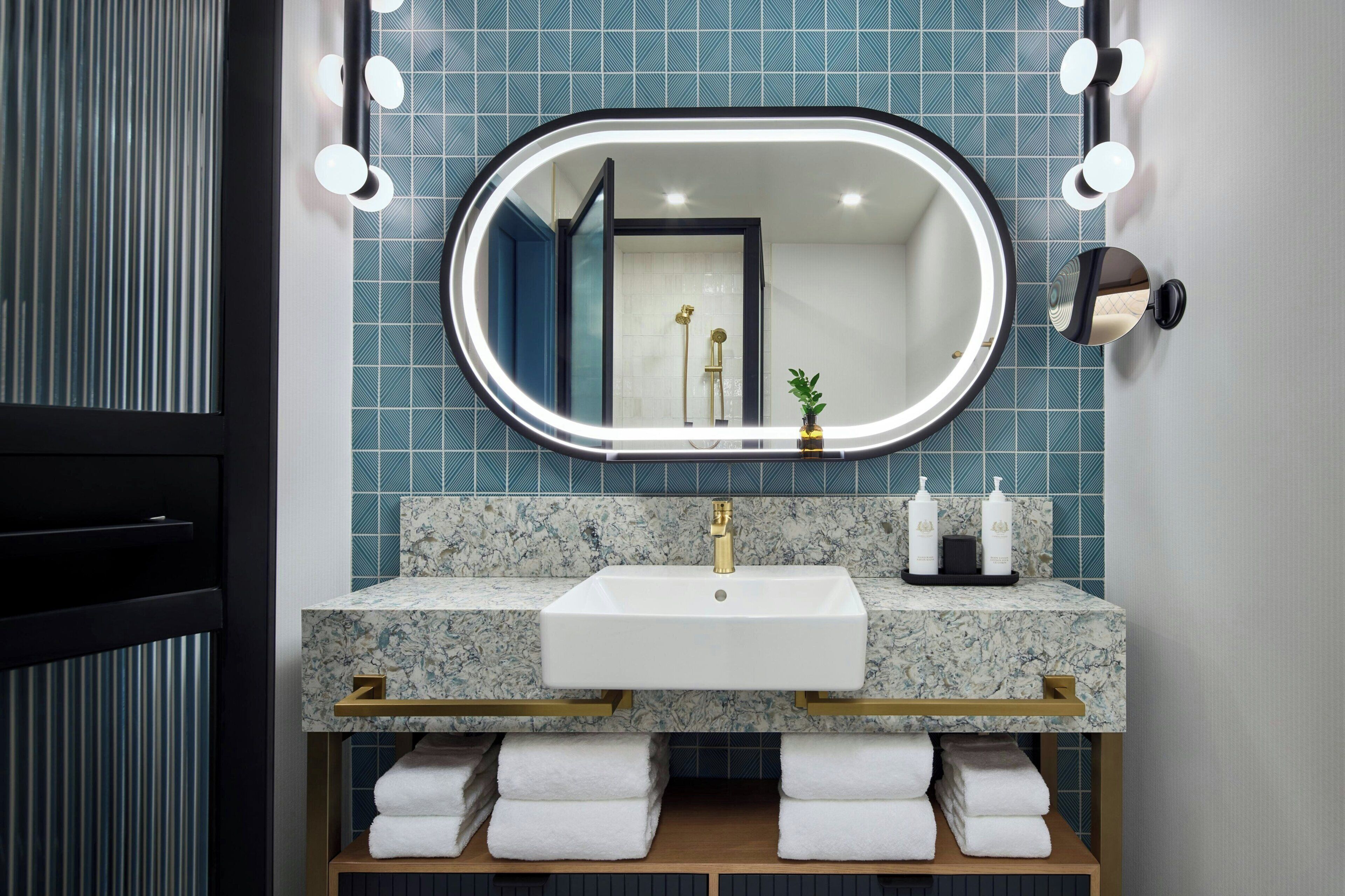 Un baño con lavamanos blanco, detalles dorados y un espejo con iluminación.