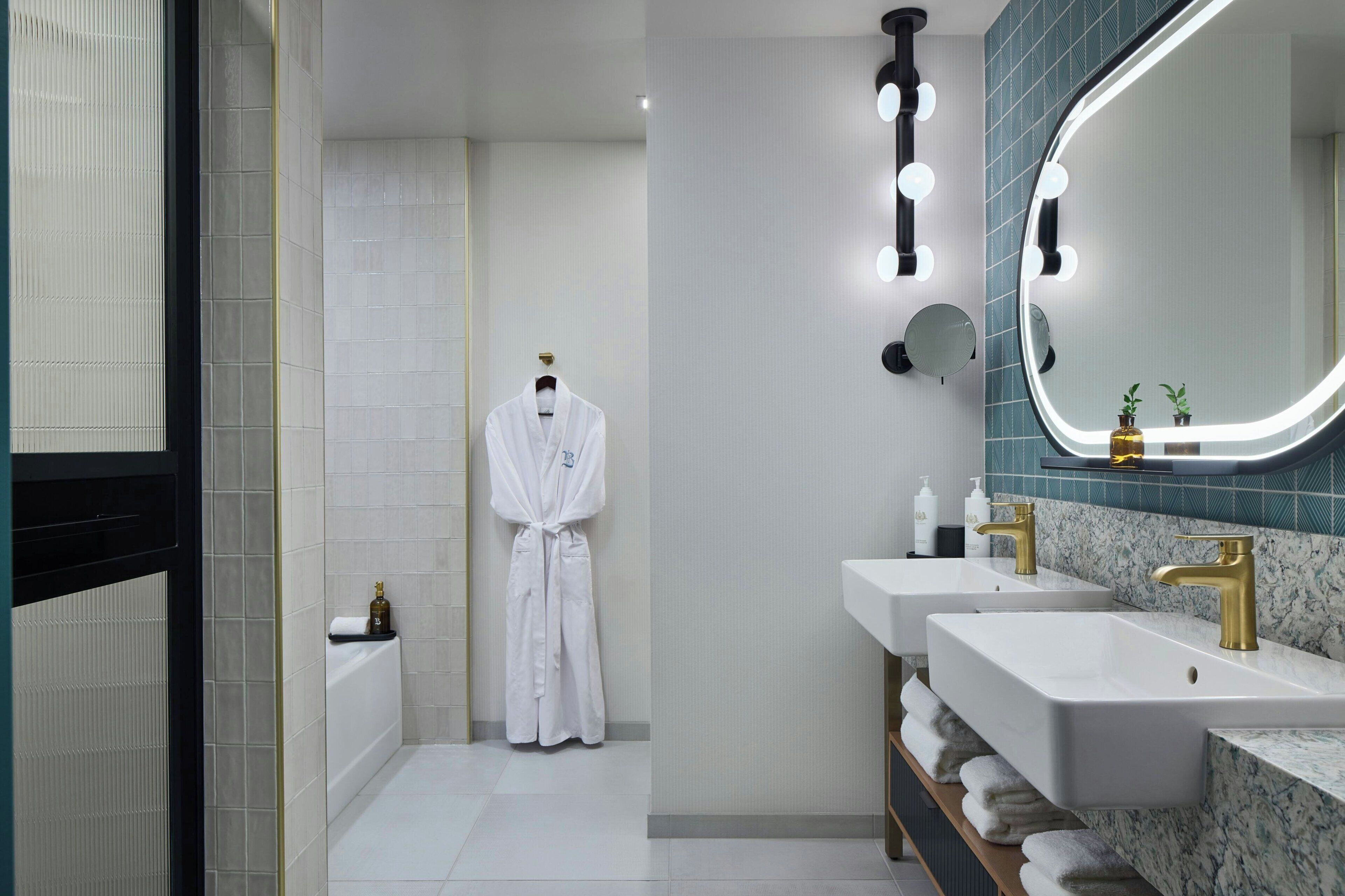 A modern bathroom with two sinks, a robe rack, and a large mirror with lights.