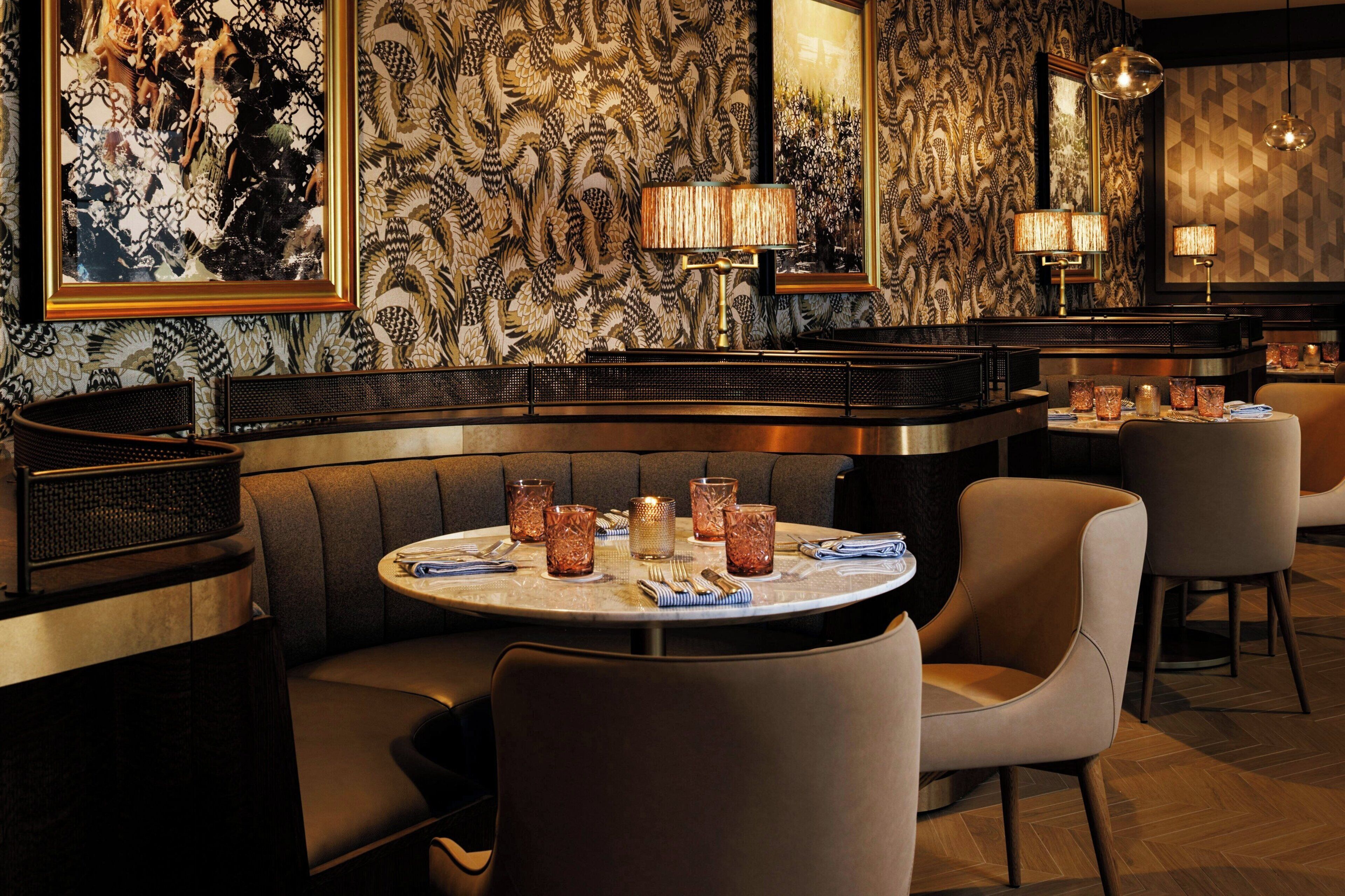 Interior de restaurante con una mesa redonda, asientos acolchados y papel tapiz estampado.