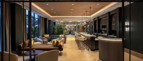 A modern hotel lobby with a bar area, seating, and a view of the cityscape.