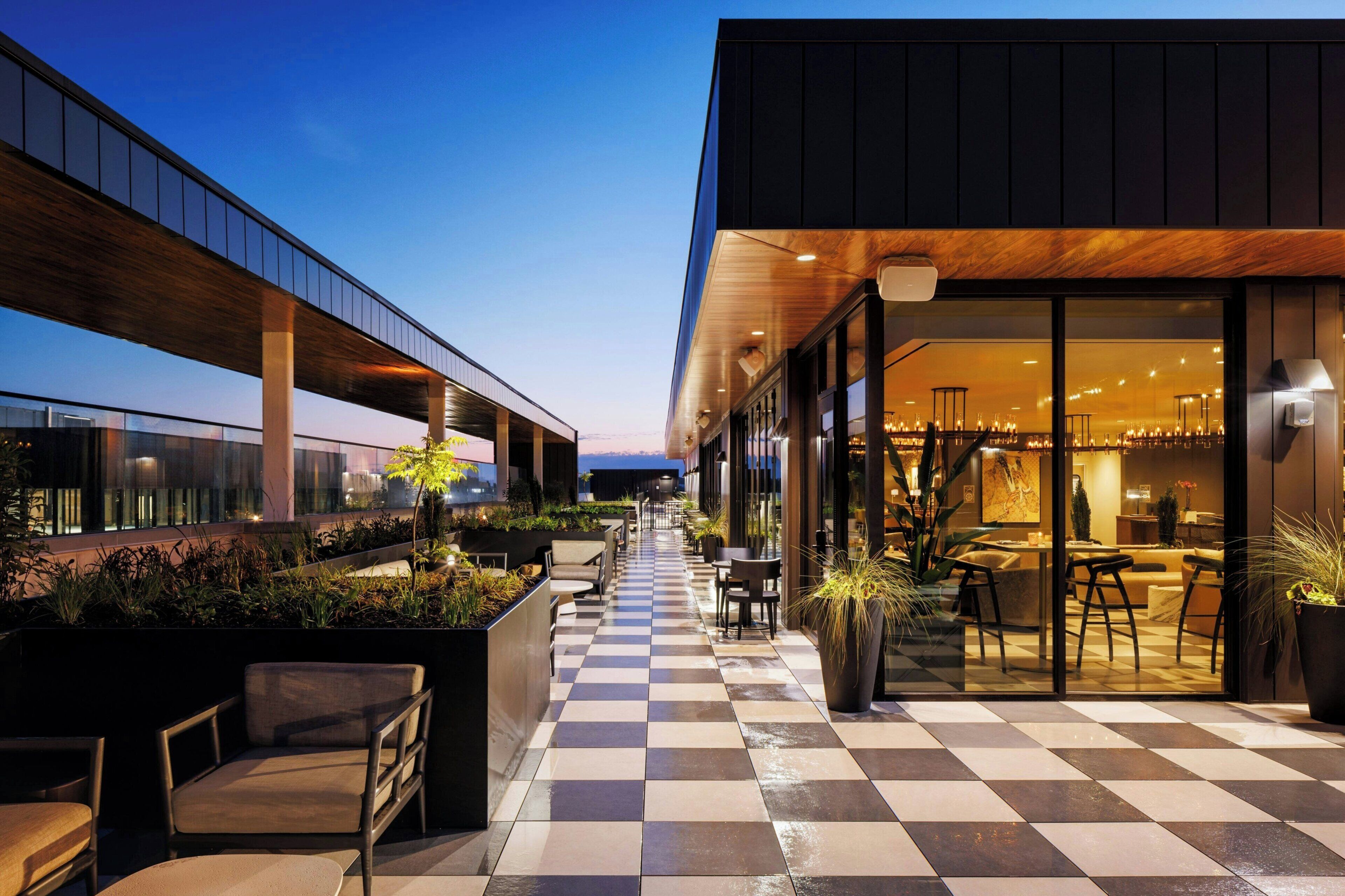 An outdoor seating area with checkered flooring, potted plants, and modern furniture.