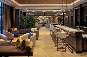 Un moderno vestíbulo de hotel con un área de descanso, un bar y vistas a la ciudad.