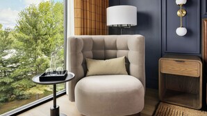 En moderne stue med et stort vindue, et rundt bord med glas, en lampe og et lille træsidebord.