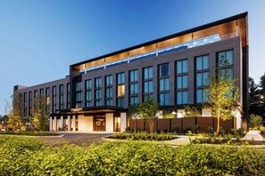 A modern hotel building with a flat facade, large windows, and a well-maintained outdoor area with greenery.