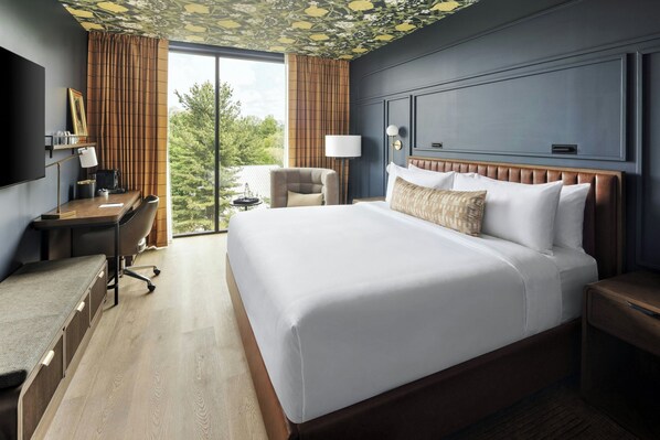 Une chambre d’hôtel avec un grand lit, un bureau avec une chaise, une télévision et une fenêtre avec des rideaux.