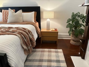 A neatly arranged bedroom with a bed, bedside table, lamp, and a potted plant.