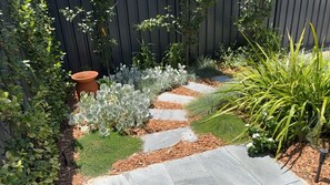 A garden pathway with stepping stones, surrounded by various plants and a wooden fence.