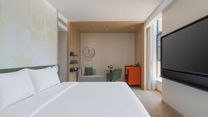 A hotel room with a bed, a desk, a chair, a TV, and a wall with a geometric pattern.