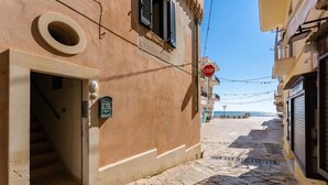 Una estrecha calle adoquinada con una señal de alto, la entrada de un edificio con escaleras, y una vista despejada del mar al fondo.