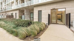 Un edificio moderno con ingresso in vetro, un giardino curato con erba alta e un design pulito e contemporaneo.