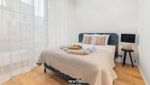 Una camera da letto ordinata con un letto, un comodino e una finestra con tende leggere.
