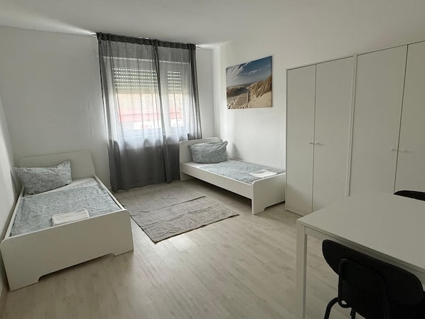 A compact bedroom with two single beds, a desk, and a wardrobe.