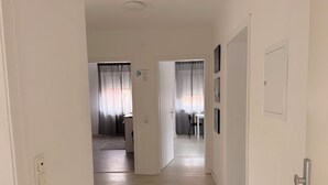 Corredor que dá acesso a uma sala de jantar, com mesa e cadeiras, geladeira e porta com fechadura.