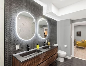 A modern bathroom with a double sink vanity, a large mirror with integrated lighting, and a toilet.