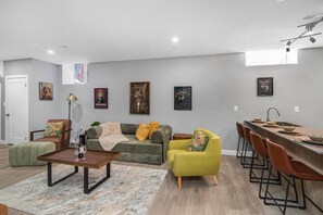 A modern living room with a sofa, armchairs, a coffee table, and a dining area with bar stools.