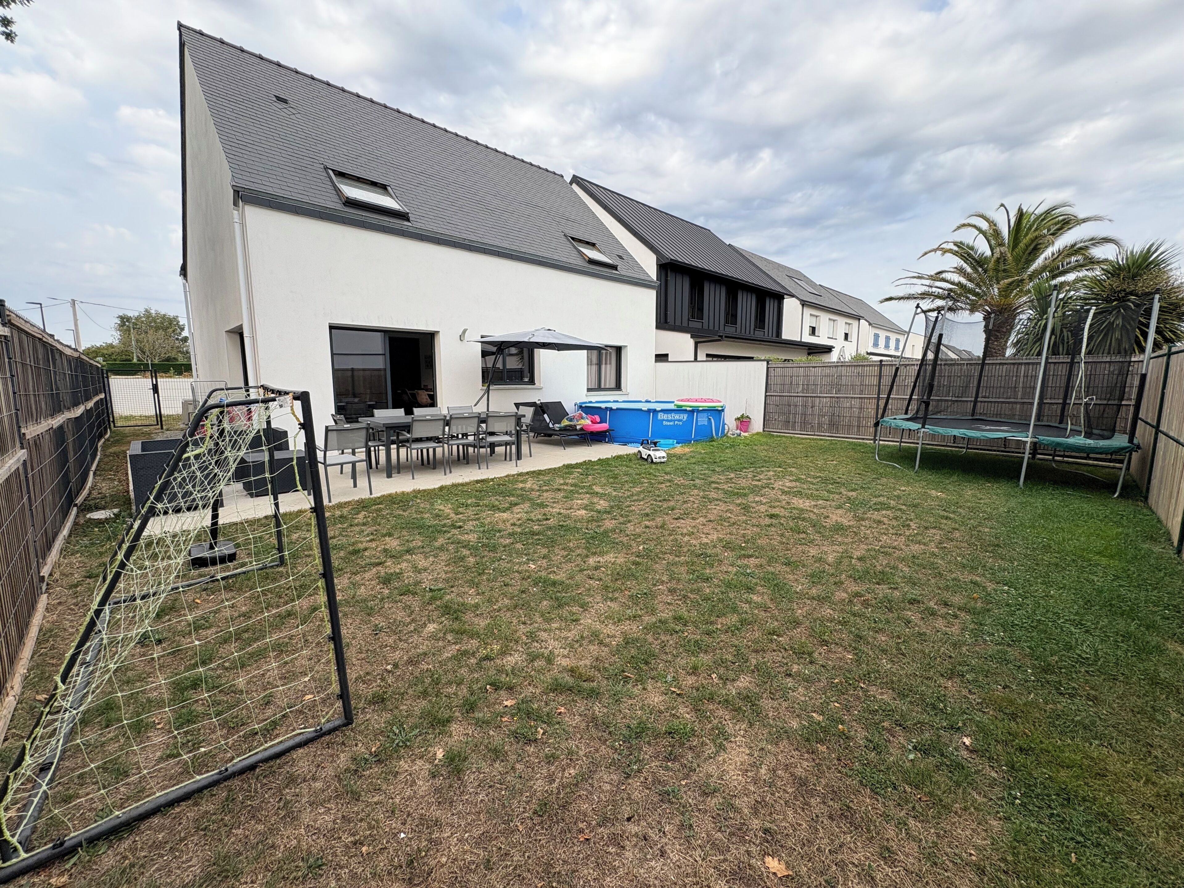 Ein modernes Haus mit einem großen Garten, einem Trampolin und einem Pool.