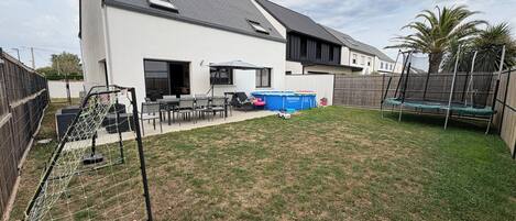 Ein modernes Haus mit einem großen Garten, einem Trampolin und einem Pool.