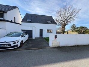 Un bâtiment blanc avec un garage, une voiture garée devant et un arbre en arrière-plan.
