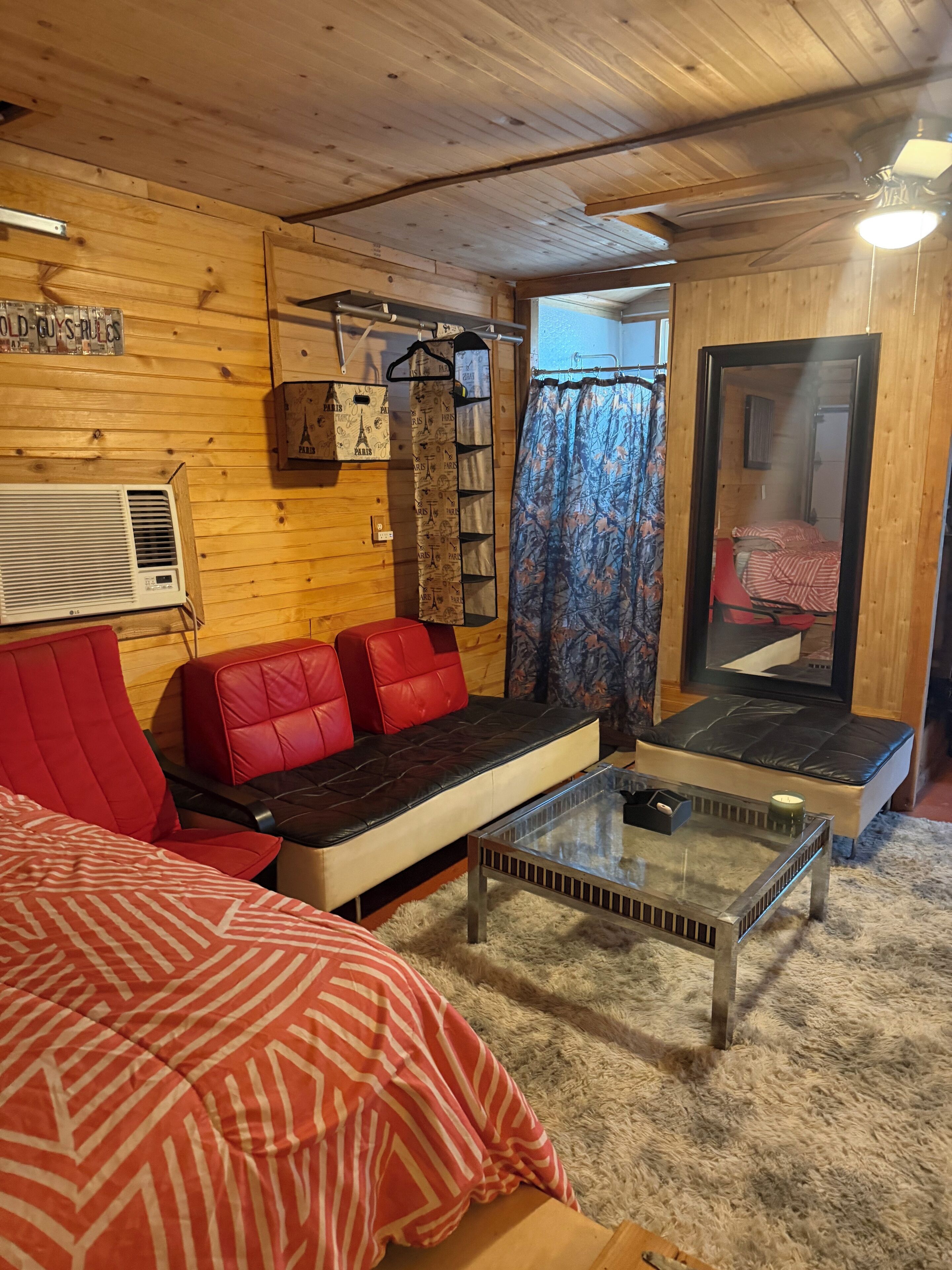 Ein gemütliches Zimmer mit Holzbalkendecke, einem roten Sofa, einem Glastisch und einem Bett mit gemustertem Überwurf.