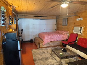 Una habitación pequeña con una cama, una silla roja, una mesita, un ventilador de techo y un calentador de pared.
