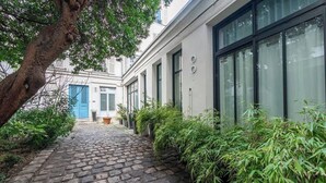 Ein Kopfsteinpflasterweg führt zu einem Gebäude mit großen Fenstern und einer blauen Tür.