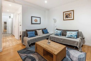 Een moderne woonkamer met twee grijze banken, een houten salontafel en een gang naar een andere kamer.