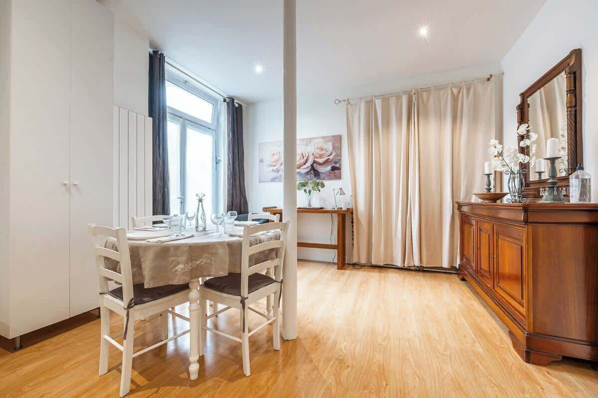 A dining area with a table set for four, a wooden cabinet, and a large window with curtains.