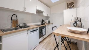 Eine moderne Küche mit weißen Schränken, einem Geschirrspüler, einem Backofen, einer Spüle, einem Wasserkocher und einem Toaster.