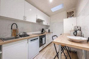 Eine moderne K üche mit weißen Schränken, einem Geschirrspüler, einem Backofen, einer Spüle, einem Wasserkocher und einem Toaster.