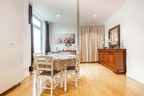 Een eetruimte met een tafel voor vier personen, een houten kast en een rozenstilleven aan de muur.