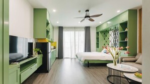 Una habitación de hotel moderna con cama, televisor, mesa de comedor y armarios verdes.