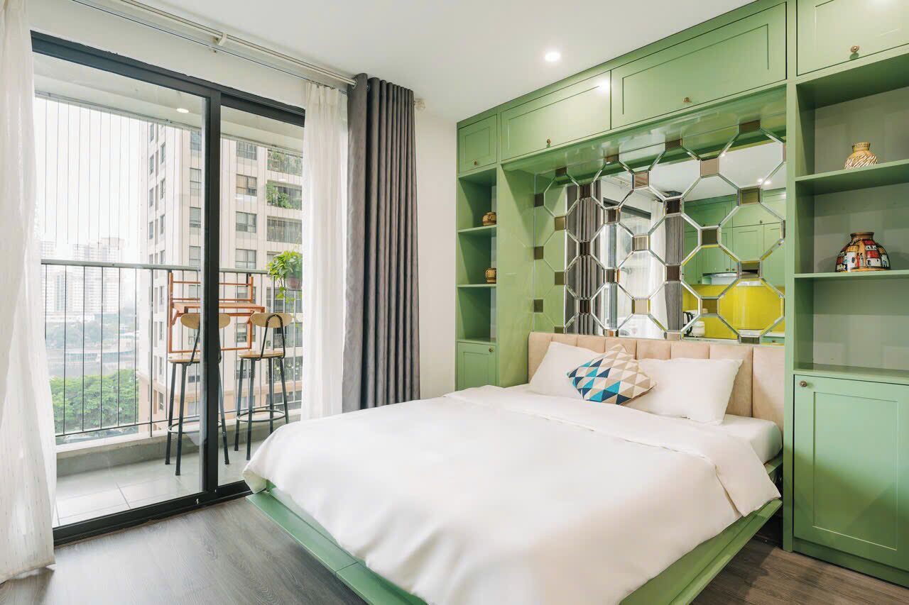 Un dormitorio moderno con una cama grande, un armario empotrado verde y un balcón con sillas y plantas.