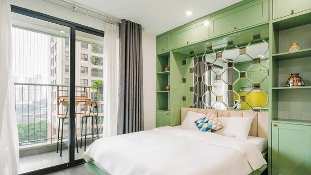 Un dormitorio moderno con una cama grande, un armario empotrado verde y un balcón con sillas y plantas.