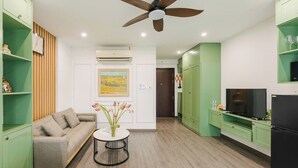 Una sala de estar moderna con un sofá, una mesita redonda con flores, un ventilador de techo y muebles de cocina verdes.