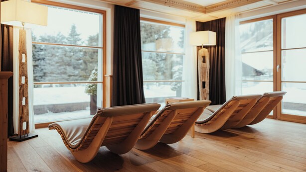 A room with wooden floors, large windows, and three reclining chairs. - Villa Flora Mountain Lodges (San Cassiano)
