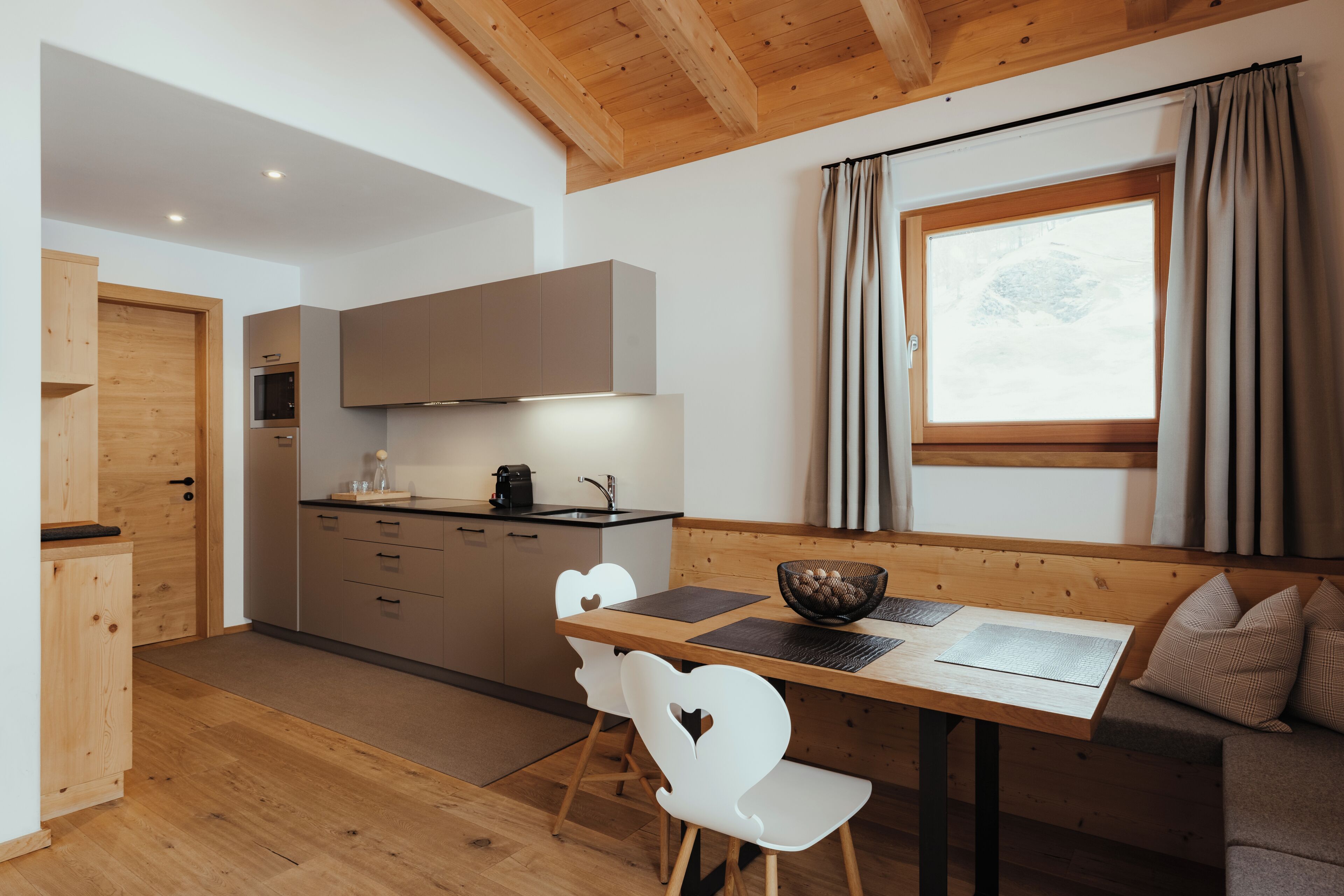 Een moderne keuken met houten kasten, een eettafel met stoelen, een raam met gordijnen en een houten plafond.